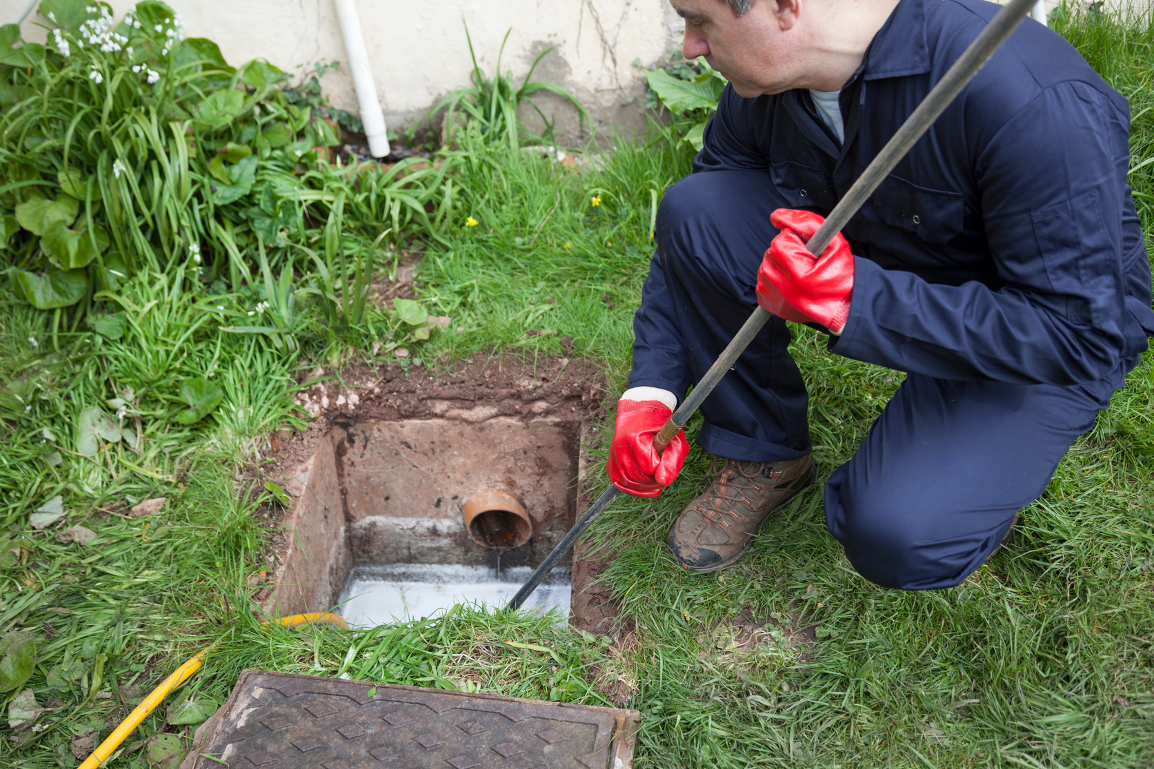 Man unblocking a drain over grass